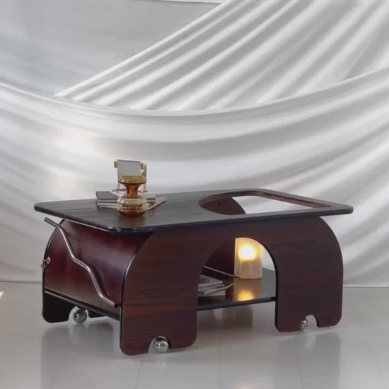 1970s dark-stained oak coffee table with sculptural curves, chrome wheels, and a sliding door storage compartment